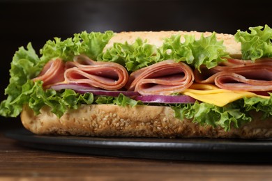 Photo of Tasty baguette sandwich with ham, cheese and vegetables on wooden table against dark background, closeup