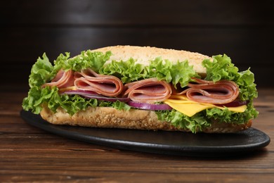 Photo of Tasty baguette sandwich with ham, cheese and vegetables on wooden table against dark background, closeup