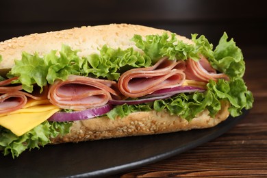 Photo of Tasty baguette sandwich with ham, cheese and vegetables on wooden table against dark background, closeup