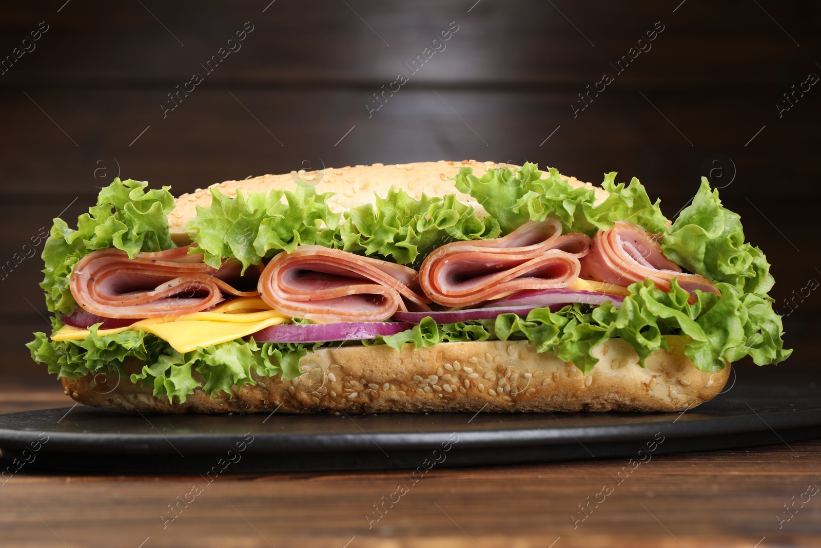 Tasty baguette sandwich with ham, cheese and vegetables on wooden table against brown background, closeup Photo of Tasty baguette sandwich with ham, cheese and vegetables on wooden table against brown background, closeup
