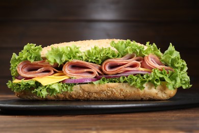 Photo of Tasty baguette sandwich with ham, cheese and vegetables on wooden table against brown background, closeup