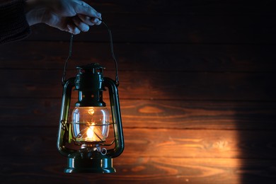 Photo of Woman holding vintage kerosene lantern near wooden wall, closeup. Space for text
