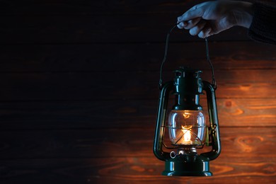 Photo of Woman holding vintage kerosene lantern near wooden wall, closeup. Space for text