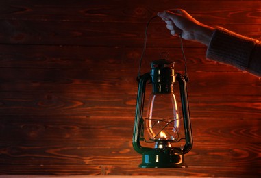 Photo of Woman holding vintage kerosene lantern near wooden wall, closeup. Space for text