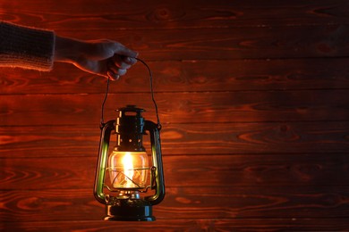 Photo of Woman holding vintage kerosene lantern near wooden wall, closeup. Space for text