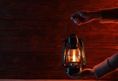 Photo of Woman holding vintage kerosene lantern near wooden wall, closeup. Space for text