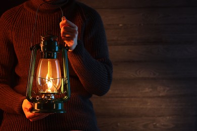 Photo of Man holding vintage kerosene lantern near wooden wall, closeup. Space for text