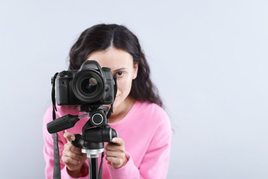 Photo of Woman with professional video camera on light grey background, selective focus. Space for text