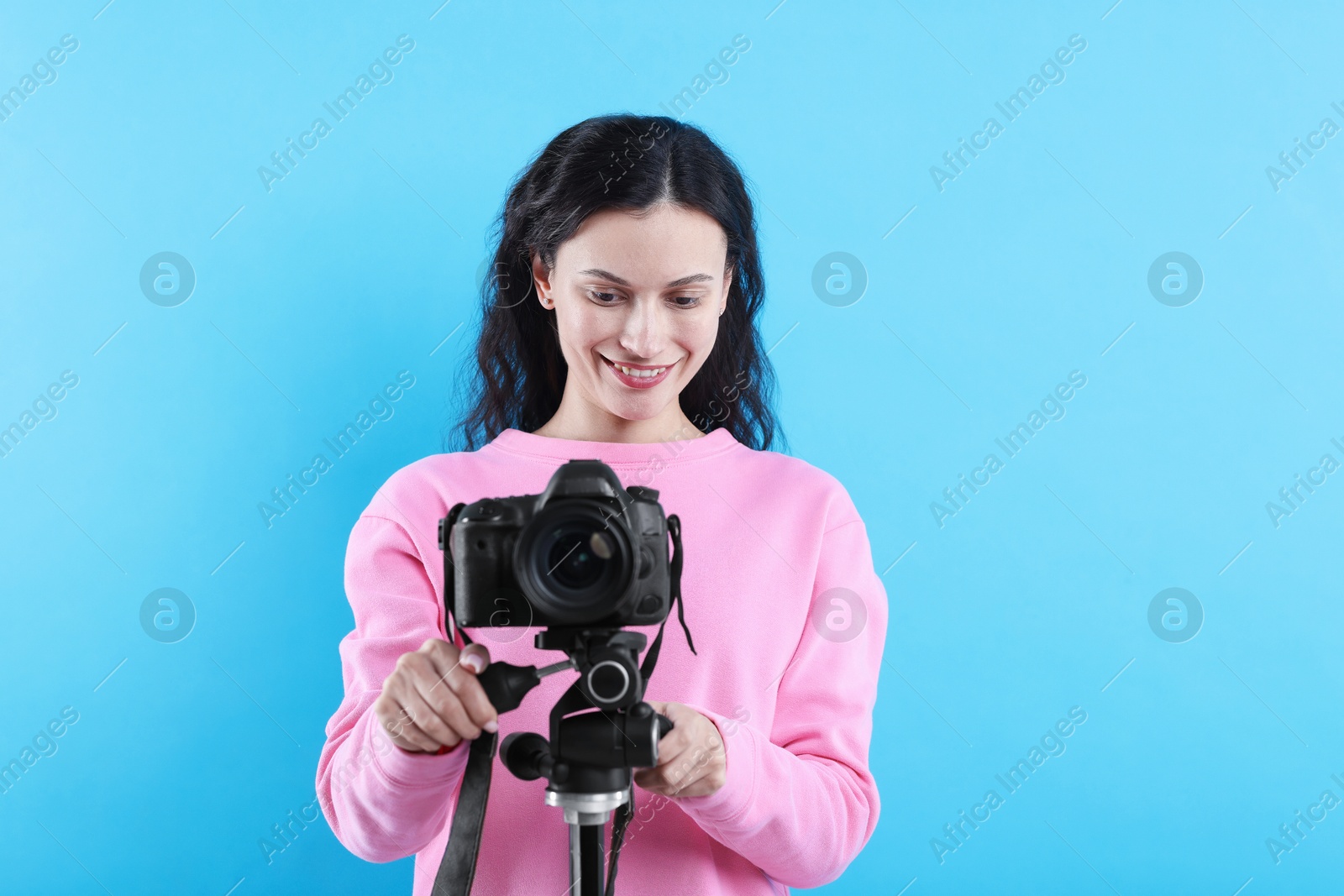 Woman with professional video camera on light blue background Photo of Woman with professional video camera on light blue background
