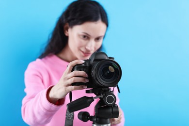 Photo of Woman with professional video camera on light blue background, selective focus. Space for text