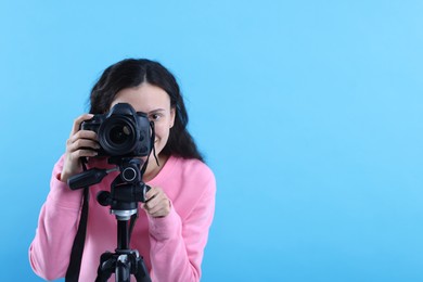 Photo of Woman with professional video camera on light blue background, space for text