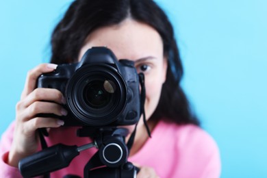 Photo of Woman with professional video camera on light blue background, selective focus
