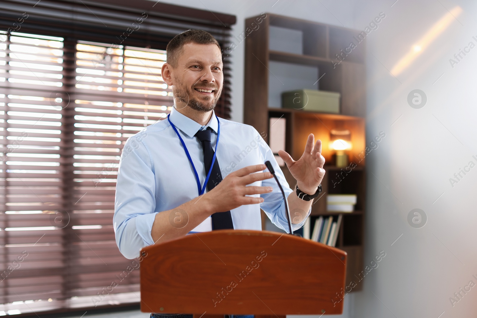 Man giving public speech with microphone at lectern indoors Photo of Man giving public speech with microphone at lectern indoors