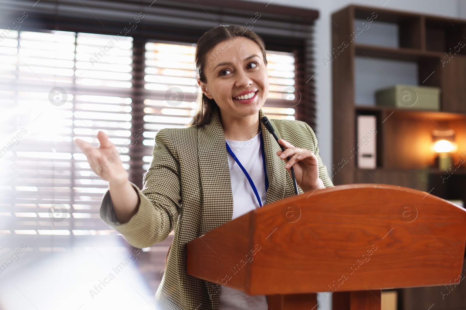 Woman giving public speech with microphone at lectern indoors Photo of Woman giving public speech with microphone at lectern indoors