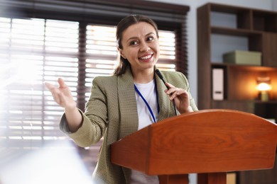 Photo of Woman giving public speech with microphone at lectern indoors