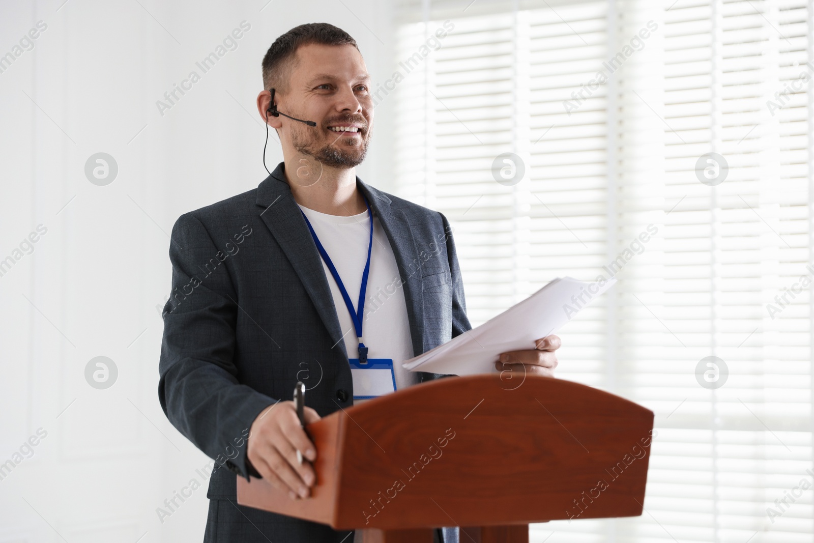 Man giving public speech with microphone at lectern indoors Photo of Man giving public speech with microphone at lectern indoors