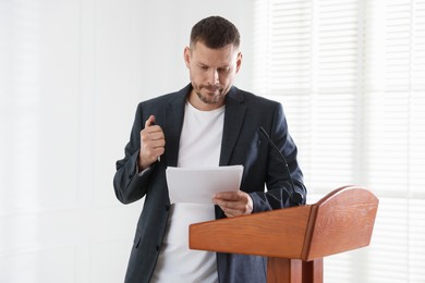 Photo of Fear of public speaking. Nervous man with microphone at lectern indoors