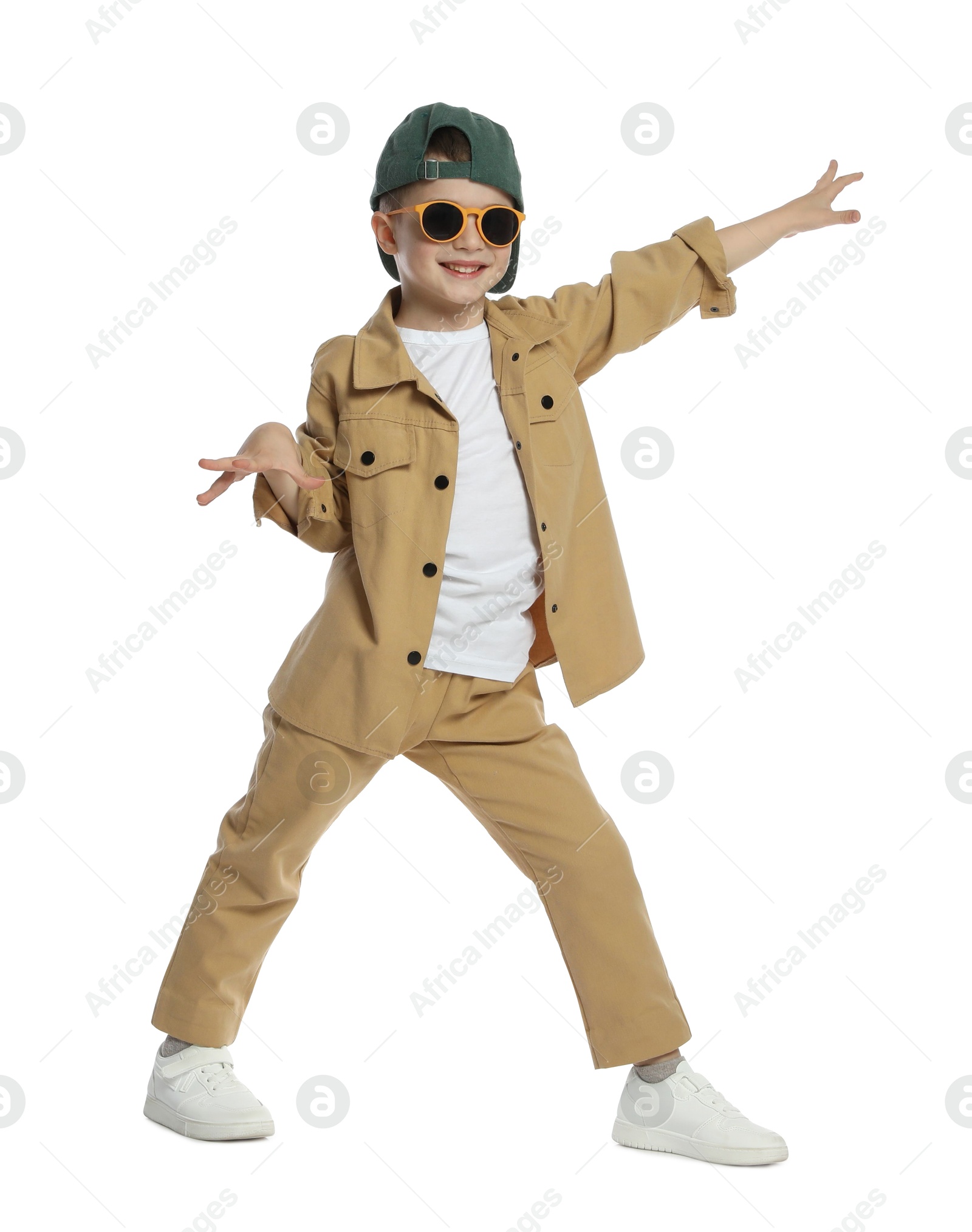 Photo of Happy little boy in sunglasses and baseball hat dancing on white background