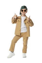 Photo of Happy little boy in stylish clothes dancing and showing thumbs up on white background