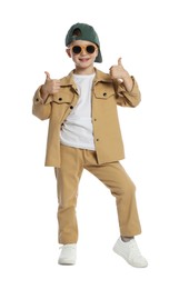 Photo of Happy little boy in stylish clothes dancing and showing thumbs up on white background