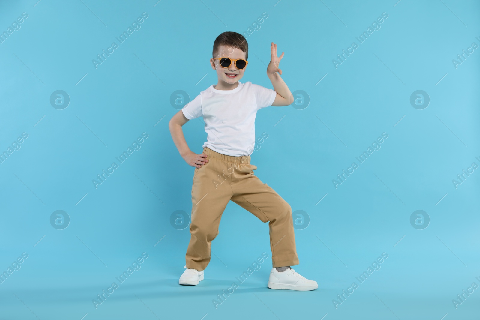 Happy little boy in sunglasses dancing on light blue background Photo of Happy little boy in sunglasses dancing on light blue background