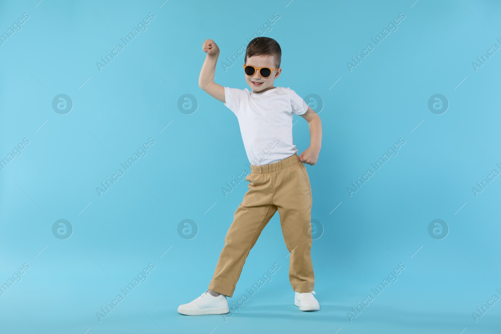 Happy little boy in sunglasses dancing on light blue background Photo of Happy little boy in sunglasses dancing on light blue background
