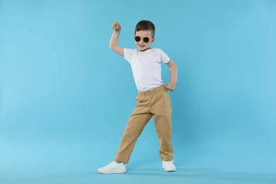 Photo of Happy little boy in sunglasses dancing on light blue background