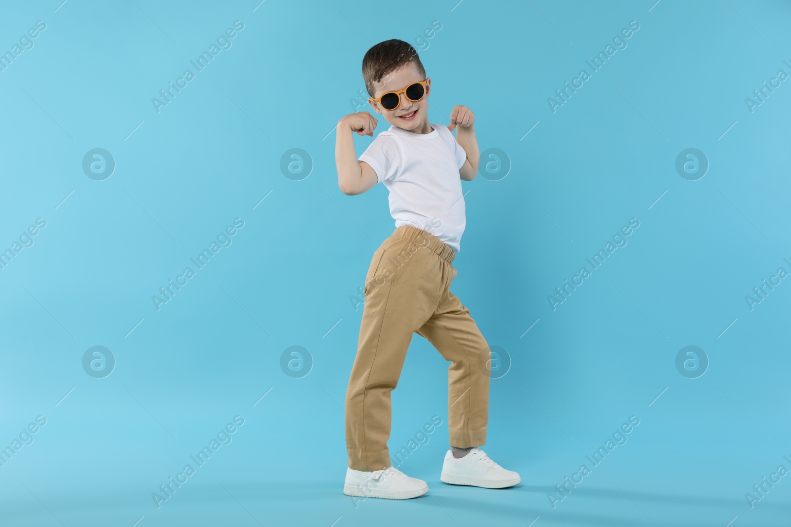 Happy little boy in sunglasses dancing on light blue background Photo of Happy little boy in sunglasses dancing on light blue background