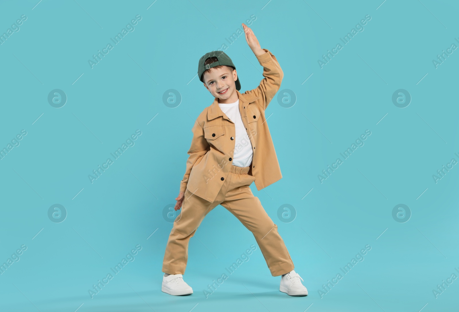 Happy little boy in baseball hat dancing on light blue background Photo of Happy little boy in baseball hat dancing on light blue background