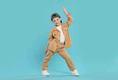 Photo of Happy little boy in baseball hat dancing on light blue background