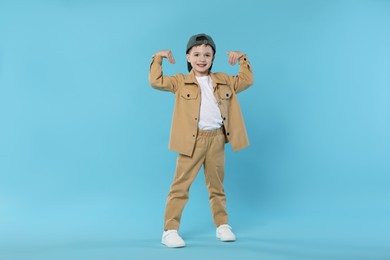 Photo of Happy little boy in baseball hat dancing on light blue background