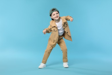 Photo of Happy little boy in baseball hat dancing on light blue background