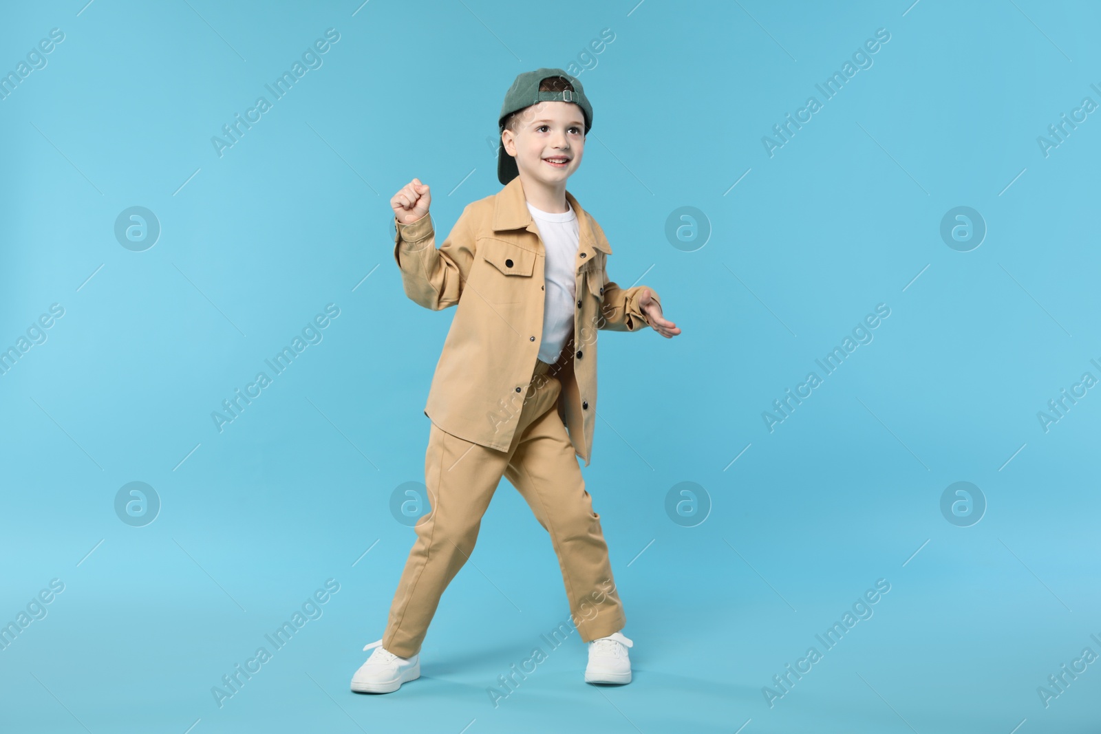 Happy little boy in baseball hat dancing on light blue background Photo of Happy little boy in baseball hat dancing on light blue background