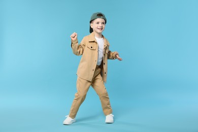 Photo of Happy little boy in baseball hat dancing on light blue background