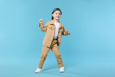 Photo of Happy little boy in baseball hat dancing on light blue background
