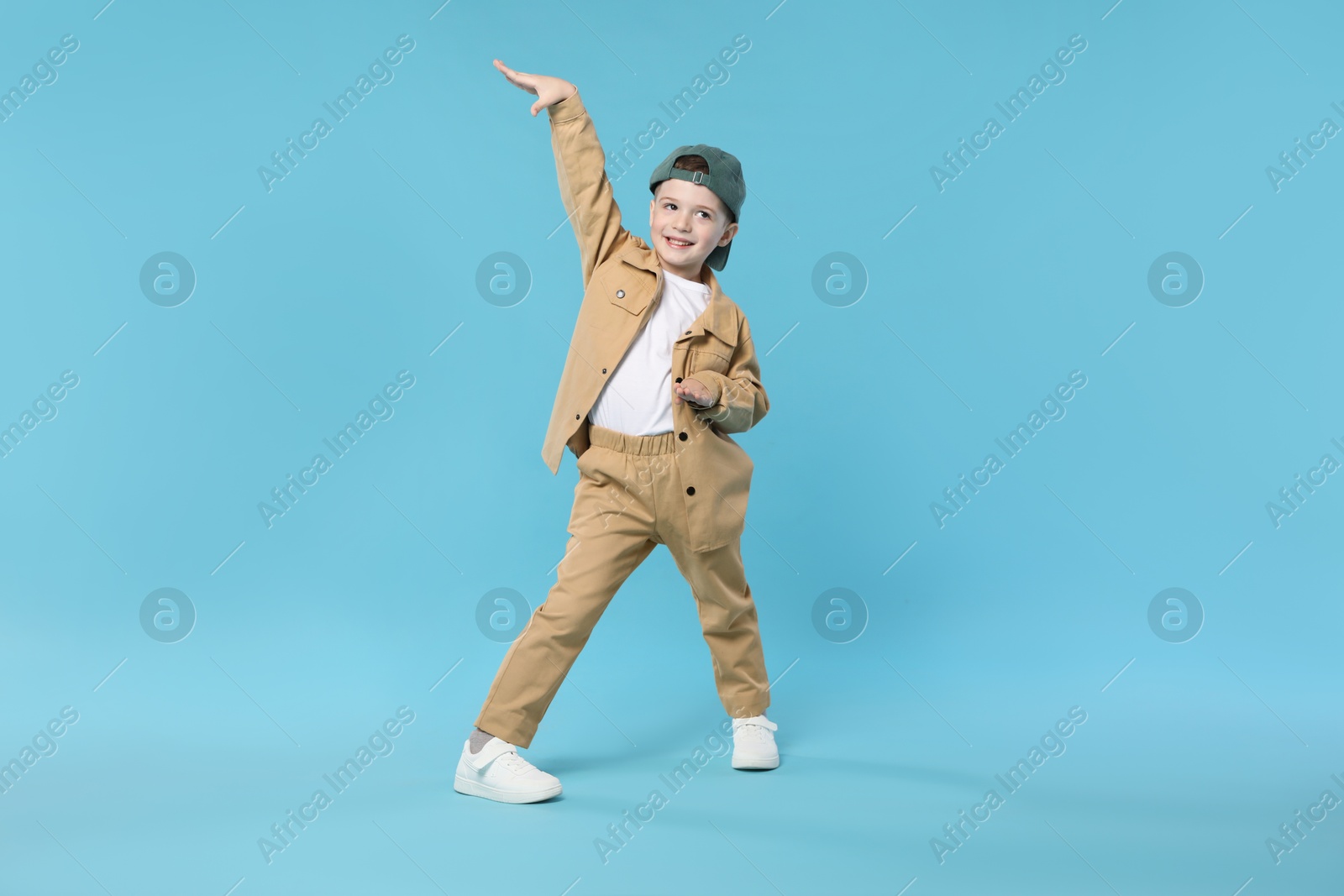 Happy little boy in baseball hat dancing on light blue background Photo of Happy little boy in baseball hat dancing on light blue background