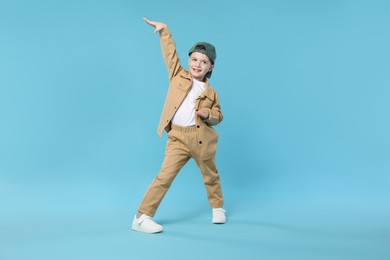 Photo of Happy little boy in baseball hat dancing on light blue background