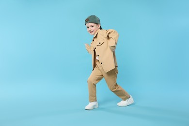 Photo of Happy little boy in baseball hat dancing on light blue background