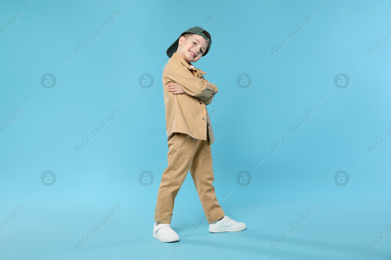 Happy little boy in baseball hat dancing on light blue background Photo of Happy little boy in baseball hat dancing on light blue background