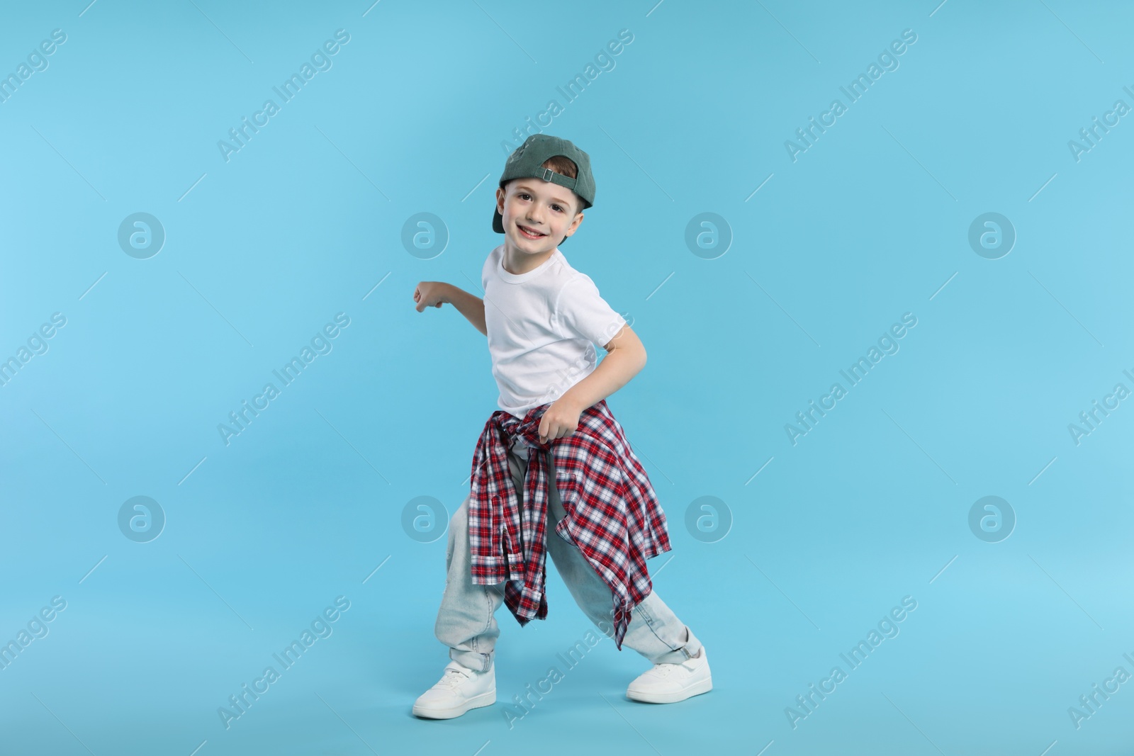 Happy little boy in baseball hat dancing on light blue background Photo of Happy little boy in baseball hat dancing on light blue background