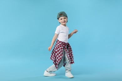 Photo of Happy little boy in baseball hat dancing on light blue background