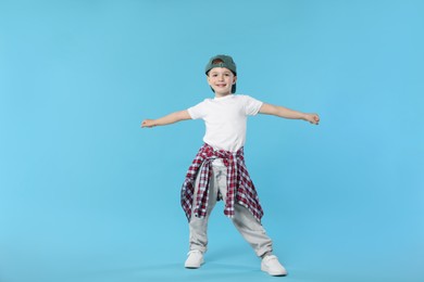 Photo of Happy little boy in baseball hat dancing on light blue background