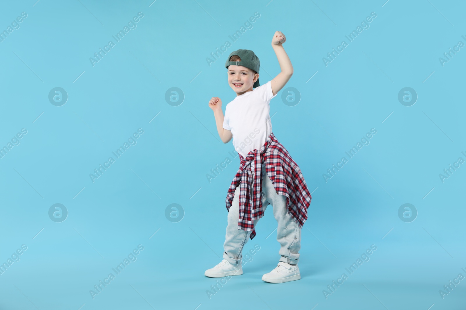Happy little boy in baseball hat dancing on light blue background Photo of Happy little boy in baseball hat dancing on light blue background