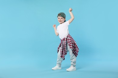Photo of Happy little boy in baseball hat dancing on light blue background