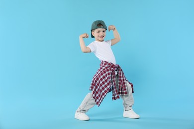 Photo of Happy little boy in baseball hat dancing on light blue background