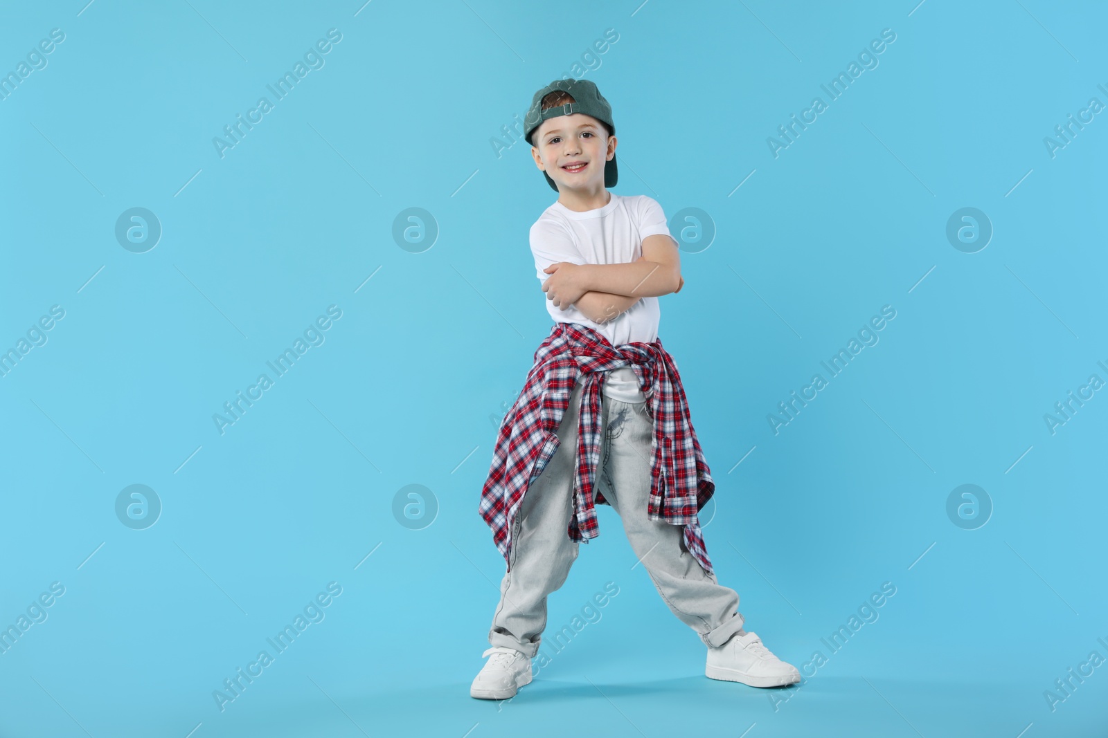 Happy little boy in baseball hat dancing on light blue background Photo of Happy little boy in baseball hat dancing on light blue background