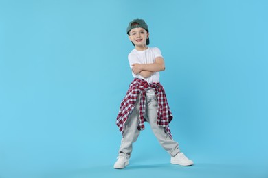 Photo of Happy little boy in baseball hat dancing on light blue background