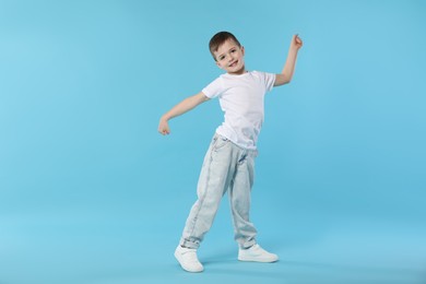 Photo of Happy little boy dancing on light blue background. Space for text