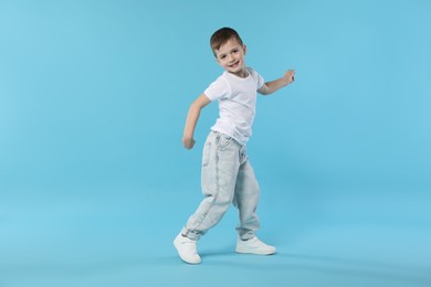 Photo of Happy little boy dancing on light blue background. Space for text