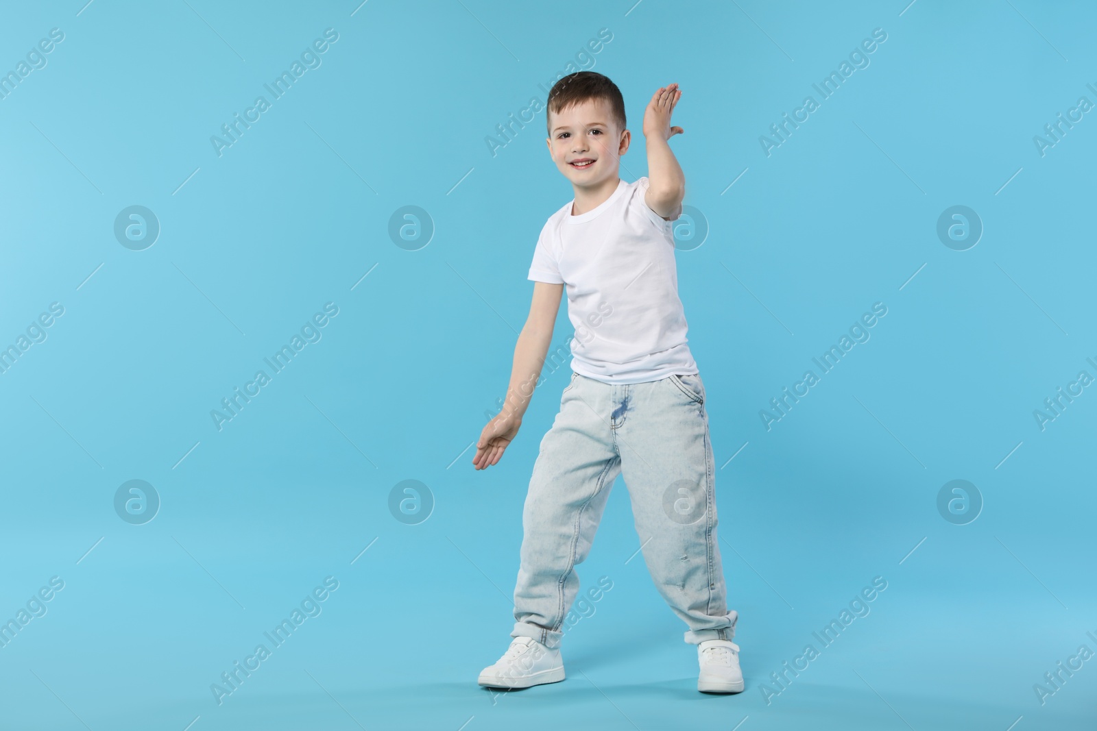 Happy little boy dancing on light blue background. Space for text Photo of Happy little boy dancing on light blue background. Space for text